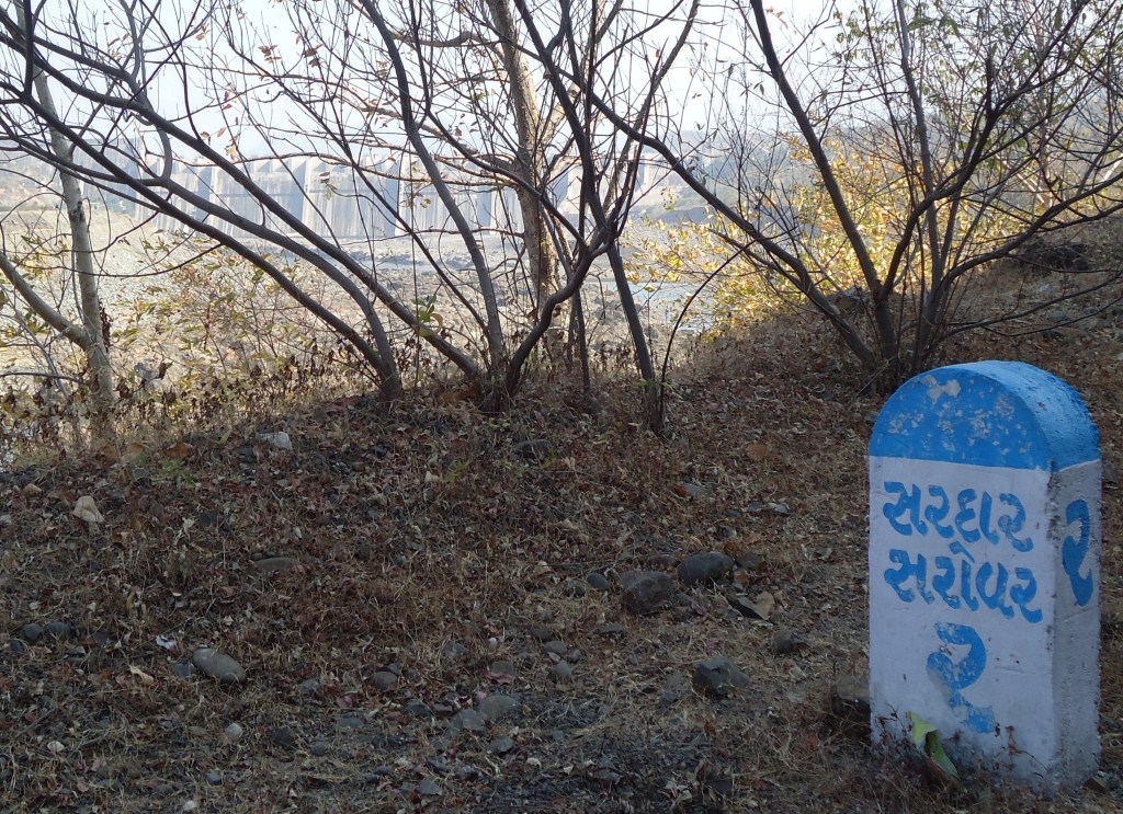 A milestone on the way to Sardar Sarovar, with the dam in the background. Photo: SANDRP